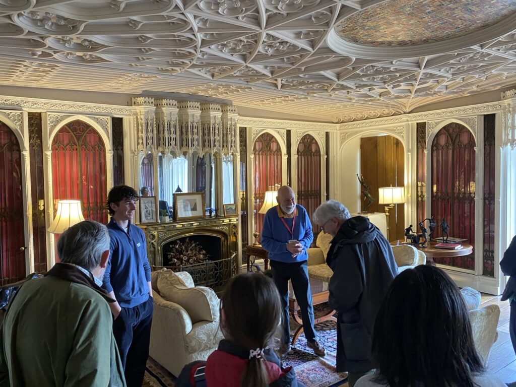 A male tour guide stands in front of a group of visitors in the Gothic Library as he tells them the history of the room.