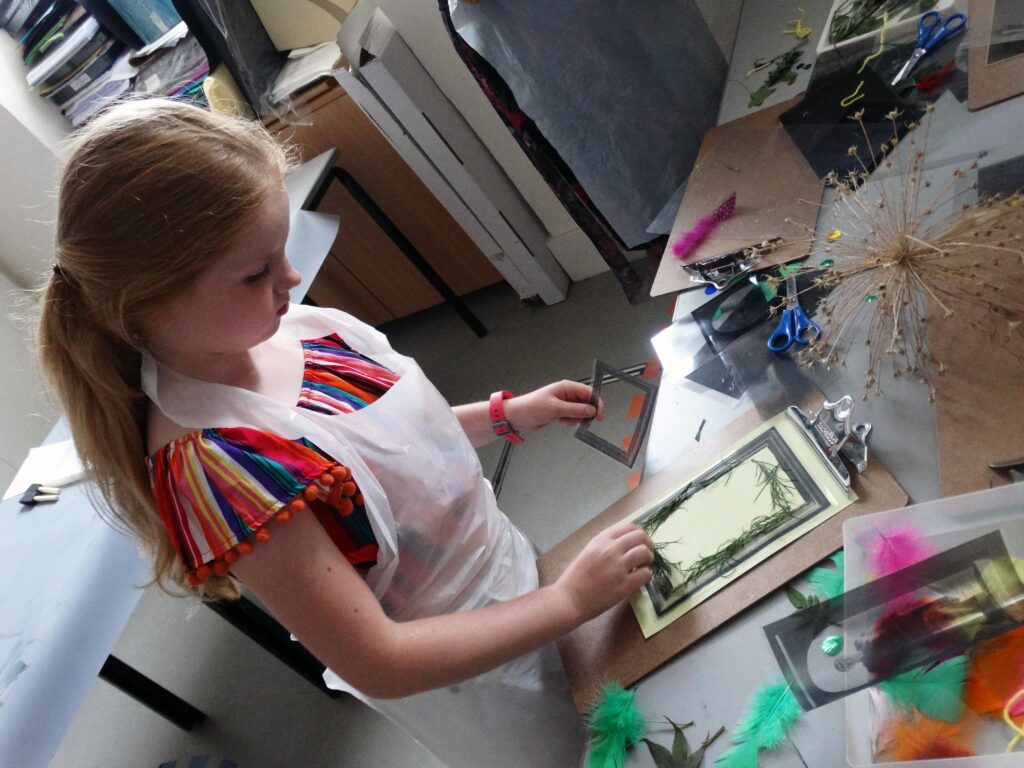 A young girl with blonde pigtails wears an apron and is doing an art activity.