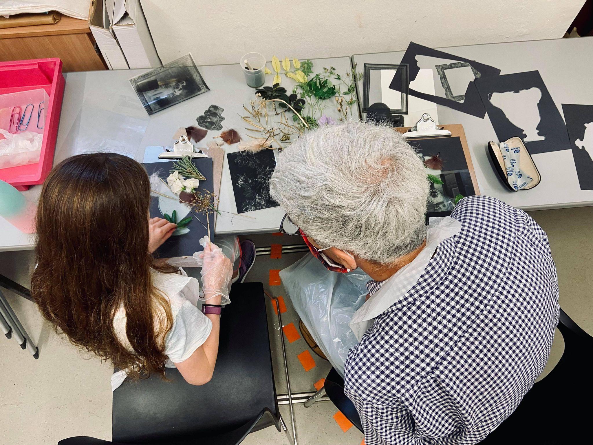 A young girl with long brown hair sits doing an art activity with an older lade with short white hair