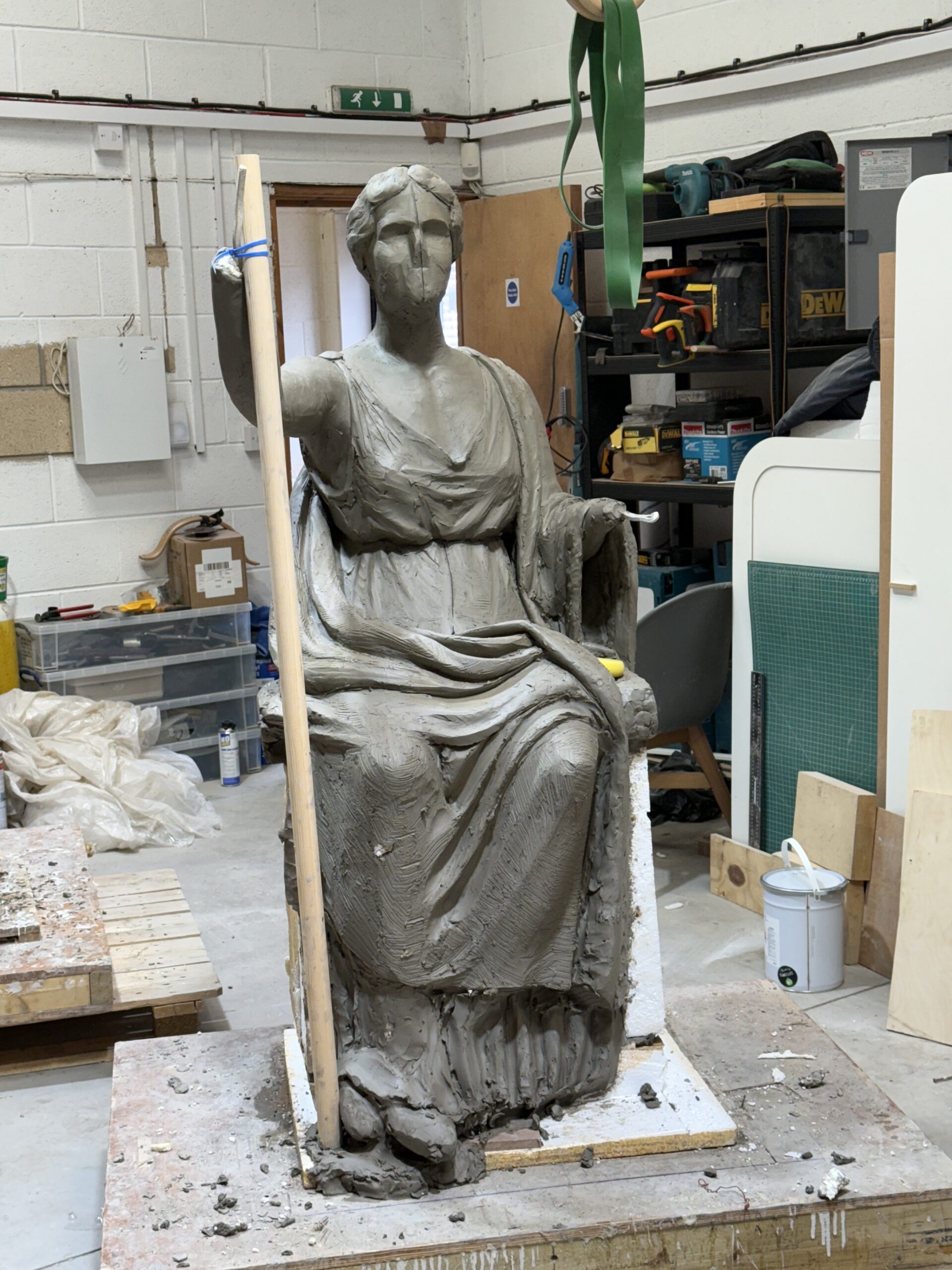 A clay model of a seated goddess holding a wooden stick