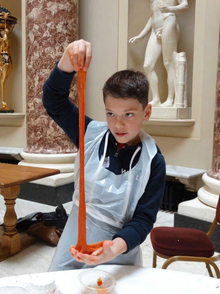 Child stretching a long strand of orange slime between their hands during a slime-making workshop at Stowe House.