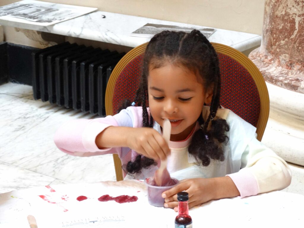 Child concentrating as she stirs purple slime in a container at the workshop table.
