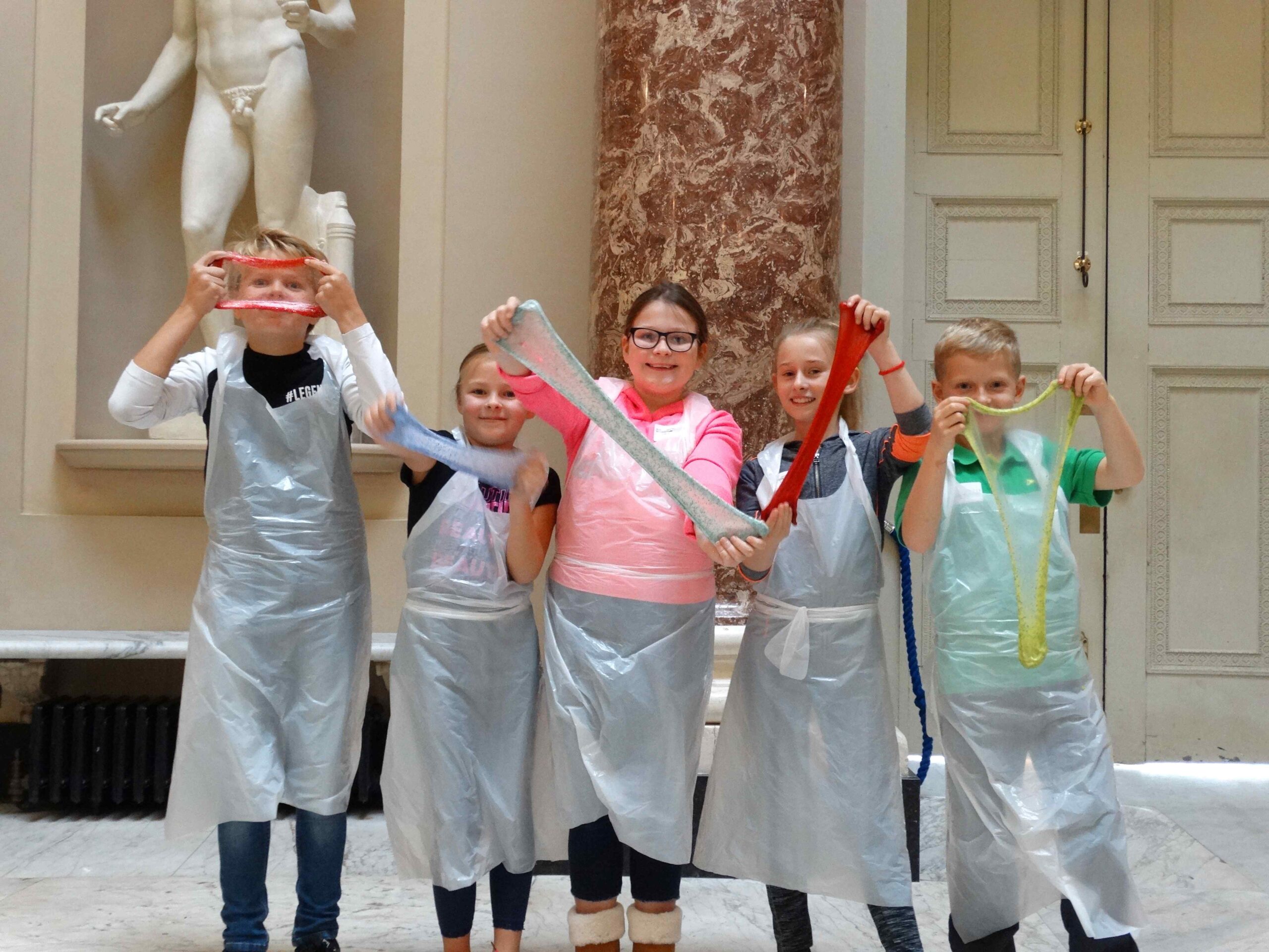 Five children proudly displaying colourful, stretchy slime creations inside Stowe House.