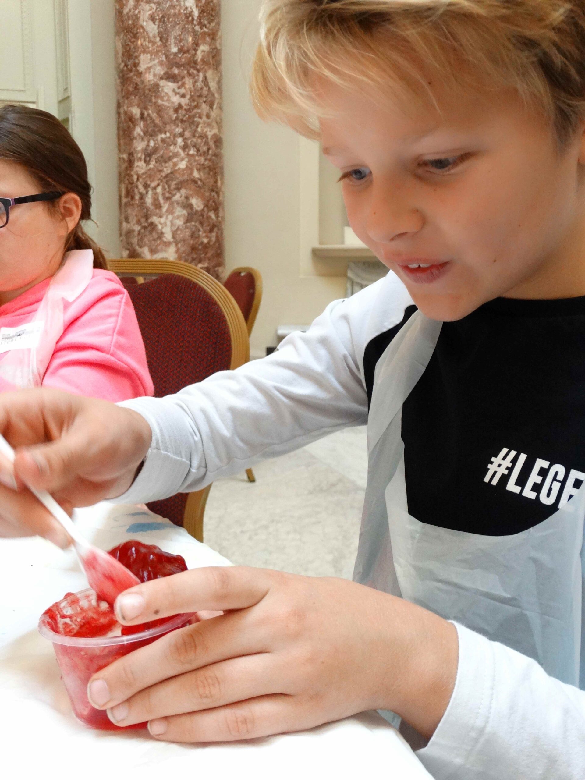 Child concentrating as he mixes bright red slime in a small container.