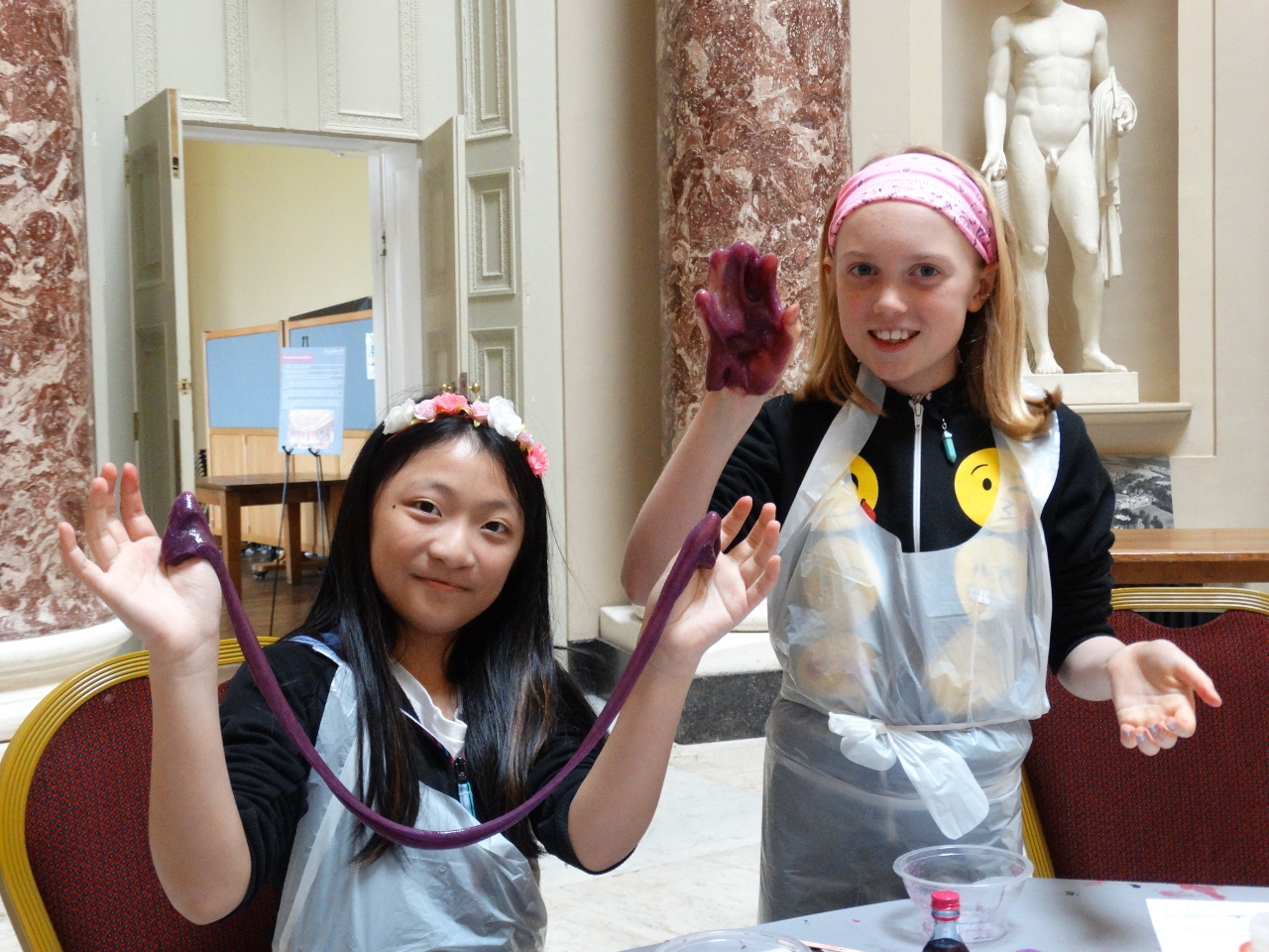 Two children smiling as they stretch and display purple slime during a workshop at Stowe House.