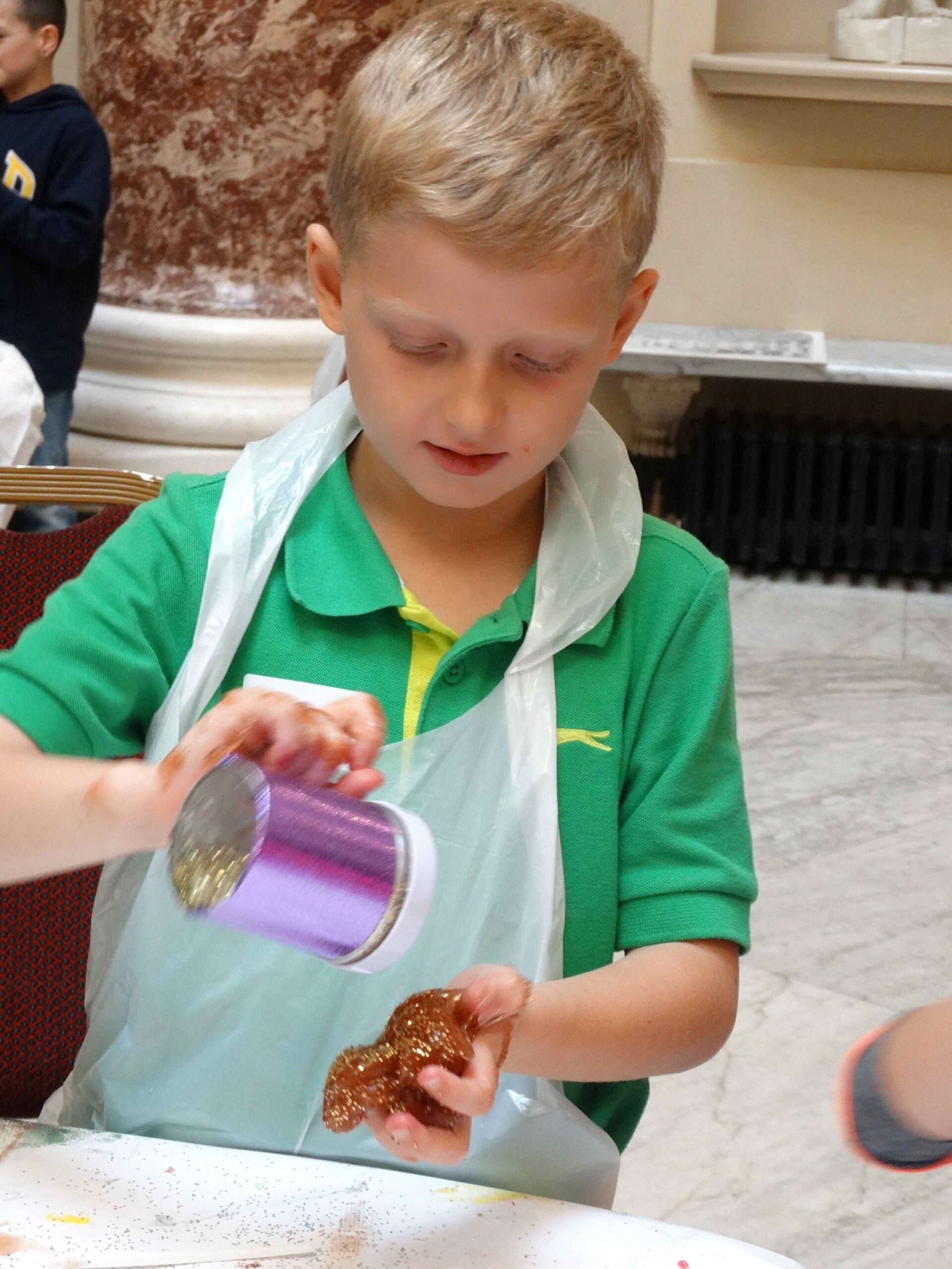 Child carefully adding glitter to a handful of brown slime during the workshop.